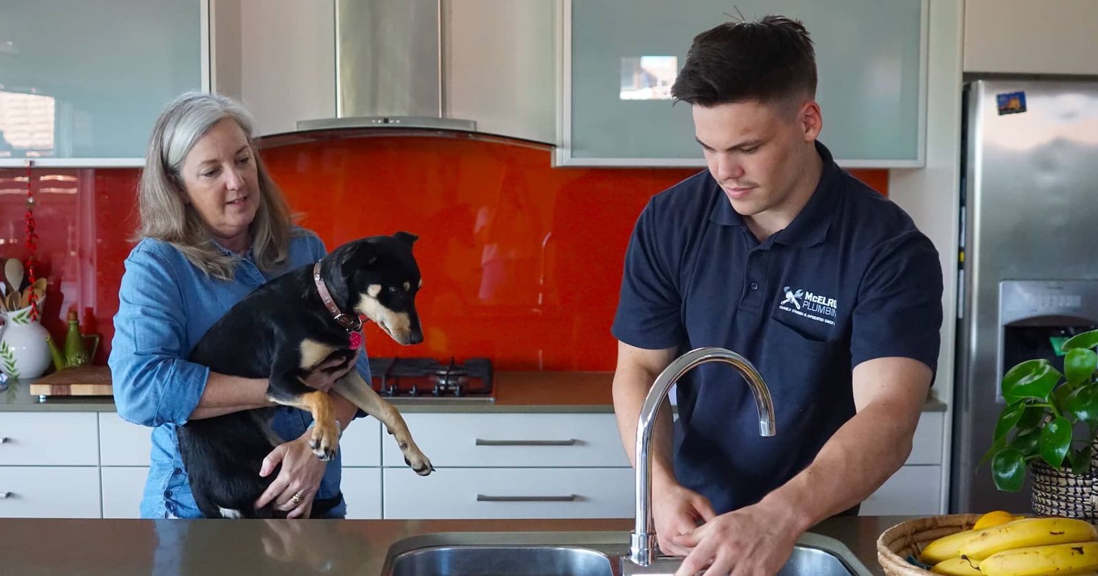 McElroy plumber fixing a kitchen tap while the owner watches with her dog